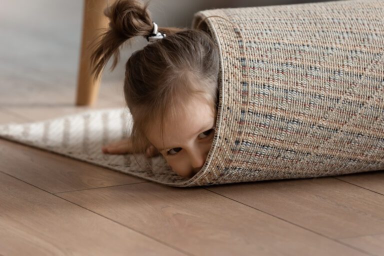 Small girl with a pigtail who has wrapped herself in a clean white rug, smiling at the camera